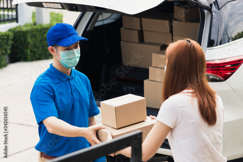 Asian young delivery man courier shopping online give parcel post box he protective face mask and service woman customer receiving boxed at front home door, under curfew pandemic coronavirus COVID-19