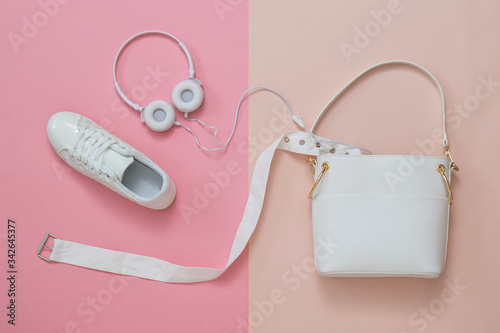 White headphones, belt and sneakers sticking out of a white bag on a pink and red background. Flat lay.