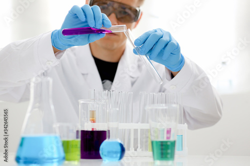 Male chemist holds test tube of glass in his hand overflows a liquid solution of potassium permanganate conducts an analysis reaction takes various versions of reagents using chemical manufacturing.