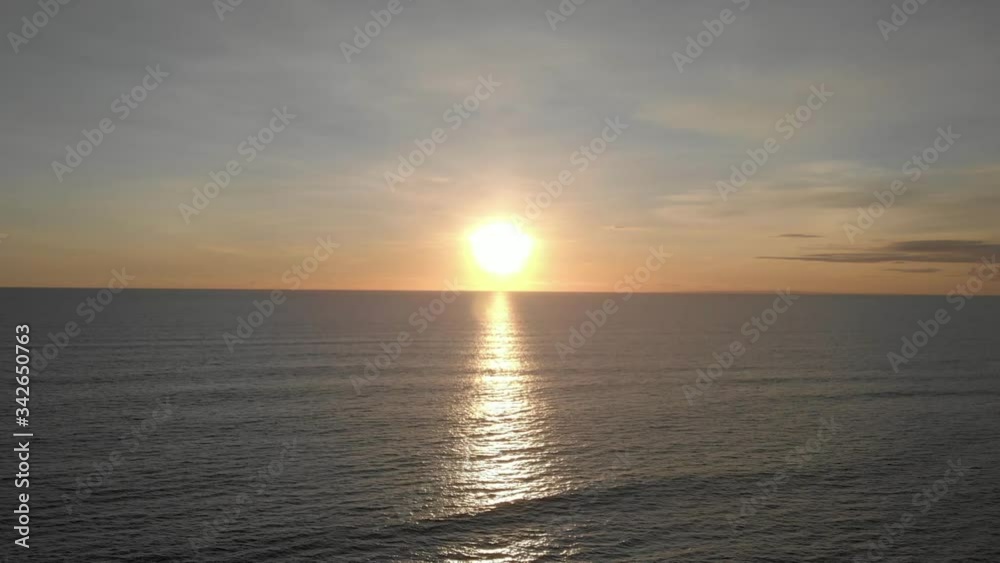 Beautiful orange sunset over the ocean. Aerial view of the ocean at summer sunset seascape. The sun touches horizon. Blue sky, yellow sun and amazing calm ocean in Bali, Indonesia Beautiful orange sunset over the ocean. Aerial view of the ocean at summer sunset seascape. The sun touches horizon. Blue sky, yellow sun and amazing calm ocean in Bali, Indonesia