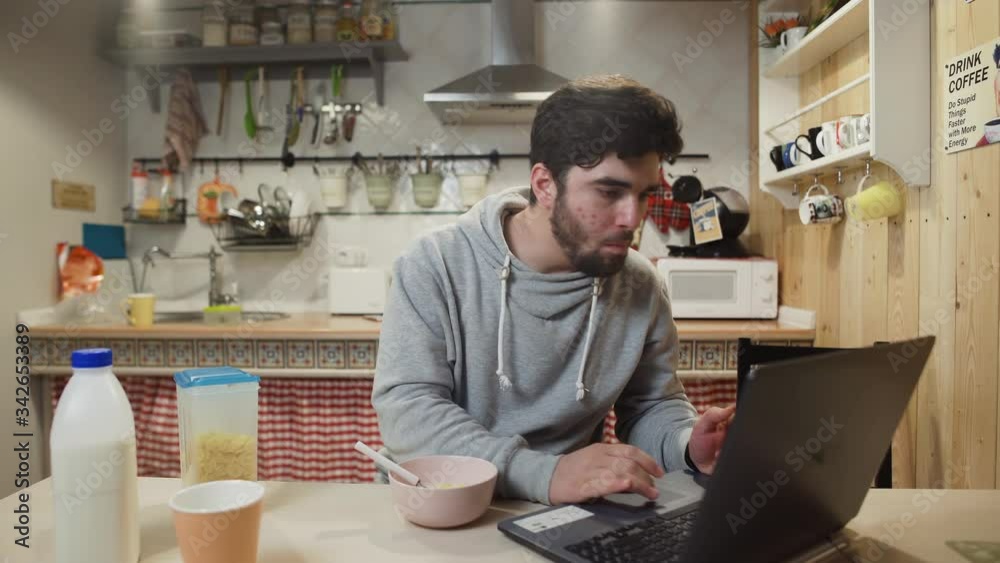 Business man working laptop computer and eats Corn Flakes Cereal at home kitchen. Business man working laptop computer and eats Corn Flakes Cereal at home kitchen.