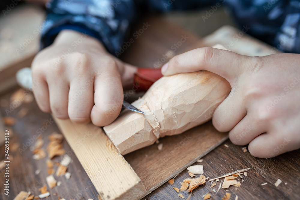 child carves a toy in wood with a knife. carpenter in the workshop. Close-up of hands