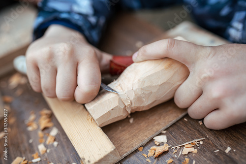 Obraz na płótnie child carves a toy in wood with a knife. carpenter in the workshop. Close-up of hands w salonie