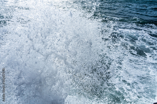 Water splashing. Crystal clear sea water beating against the rocks and cliffs. Sea waves break on the shore after a storm. Blue sky, sunny summer day, refreshing mediterranean sea water