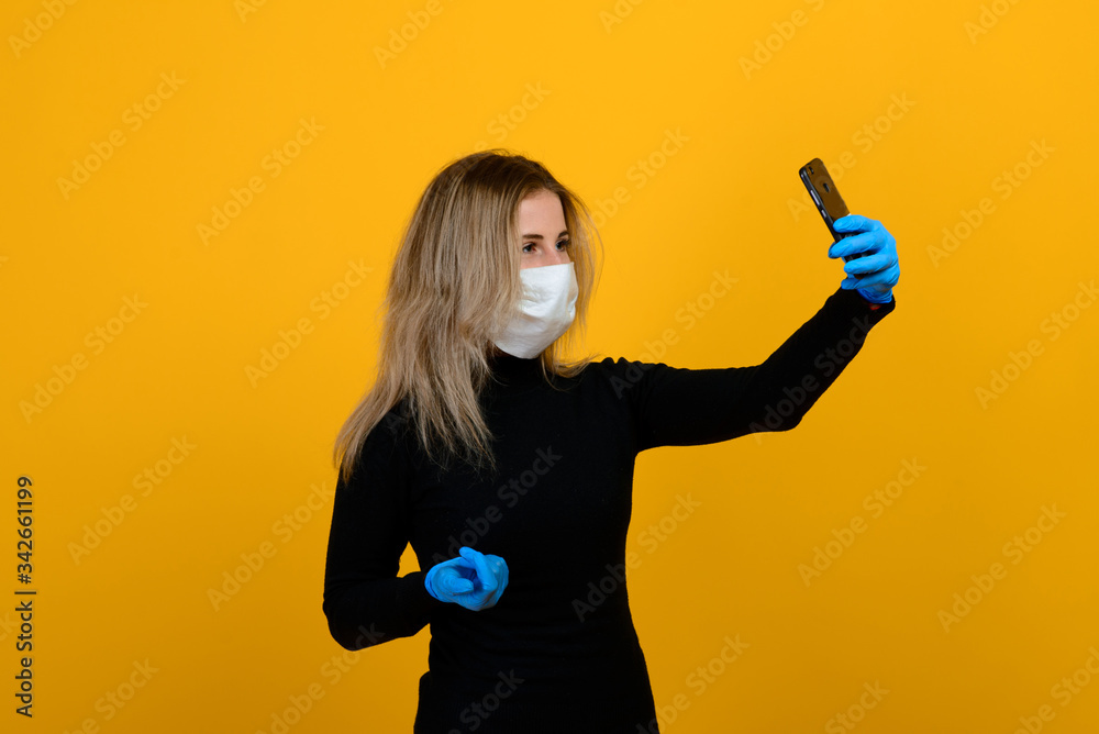Portrait of a girl in a medical mask, which puts on a rubber glove. Yellow and grey background. Copy space. Portrait of a girl in a medical mask, which puts on a rubber glove. Yellow and grey background. Copy space.