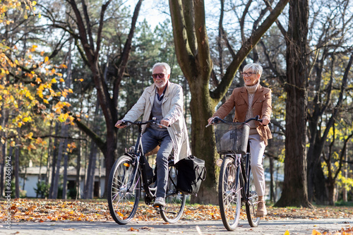 Mature fit couple ride in bicycles thru public park