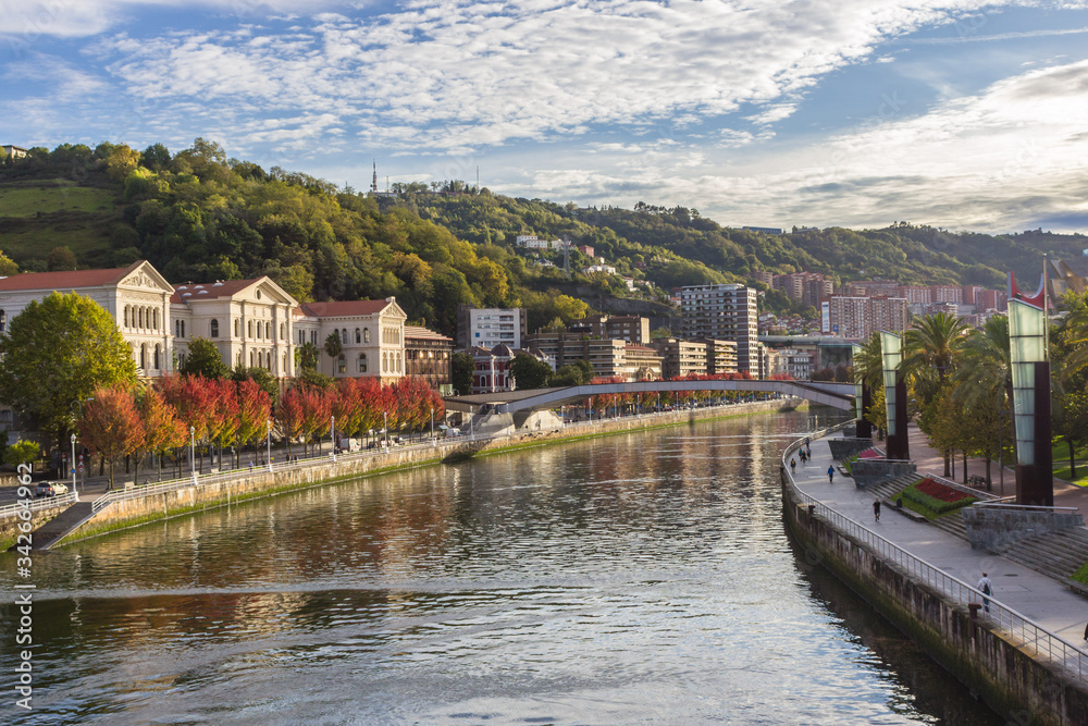 Embankment by the Nervion River in Bilbao. Bend of the river. Colors of autumn in the city. Traveling in Spain. European city. Colorful cityscape by the river. Basque Country. The large city of Spain.
