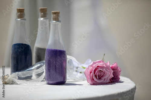 Wedding decor of bottles filled with colored sand and ribbon and pink rose for decoration on a table with white linen
