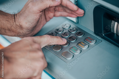 Man entering a PIN code for his credit card at an ATM, withdrawing money, finance concept photo