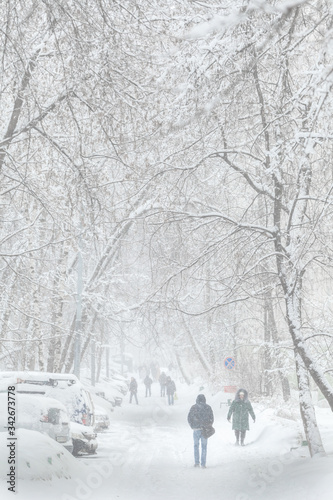 Blizzard in the city. In winter, people walk on a snow-covered road.