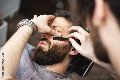  Barber hands with a razor shaving beard of male customer