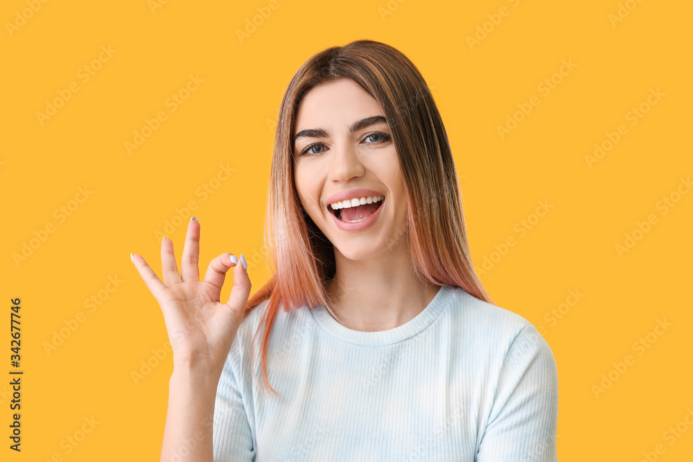 Young woman with healthy teeth showing OK gesture on color background