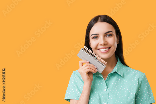 Beautiful young woman with teeth color samples on color background