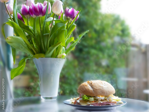 Healthy breakfast. italian bun with lettuce, cheese, ham and egg, healthy sandwich. tulips in vase in background, selective focus