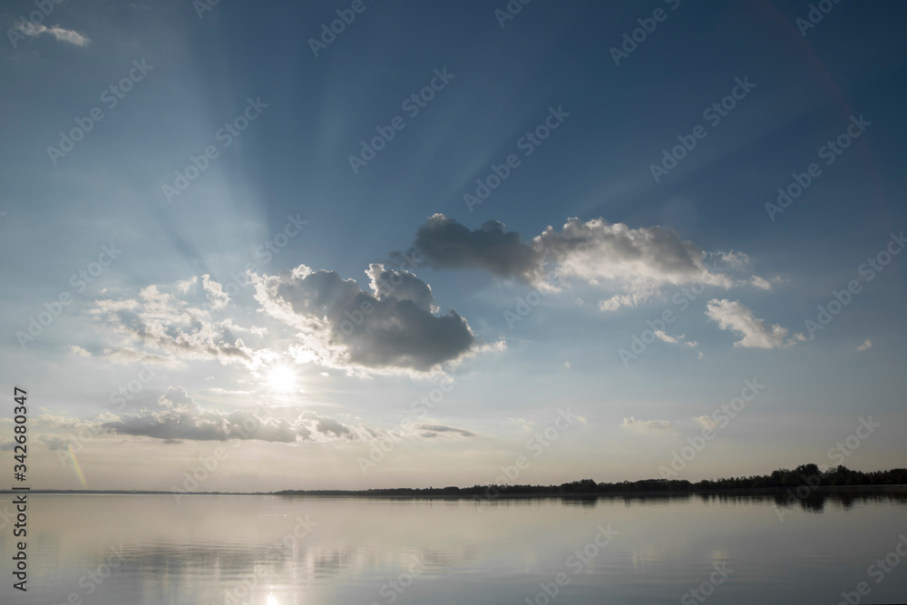 Breathtaking lake landscape at sunset / sun going down and hiding behind clouds / sunlight beams / water reflection