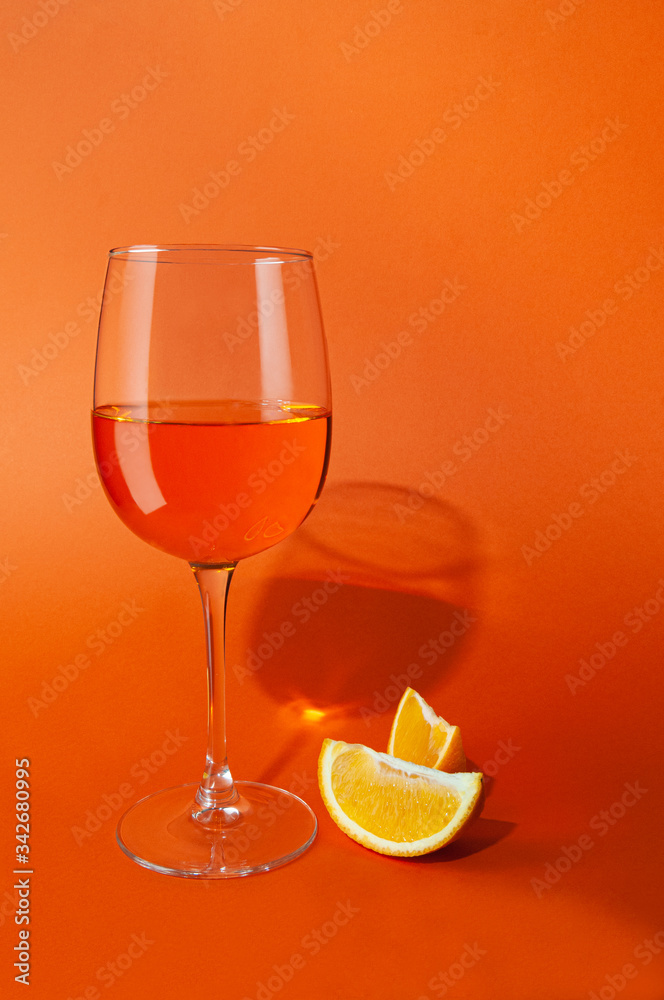 Cocktail aperol spritz. In a glass goblet. Next to the glass are two slices of orange. On a plain orange background. Hard light, sharp shadows. Close-up. Place for text.