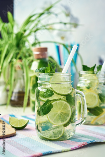 A glass of homemade lemon, lime, and mint lemonade sits on the wooden dining table. Cold, refreshing summer lemonade or mojito.