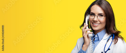 Portrait picture of happy smiling young doctor talking on phone, over orange yellow background. Copy space for some sign, slogan or advertising text. Medical call center service. photo