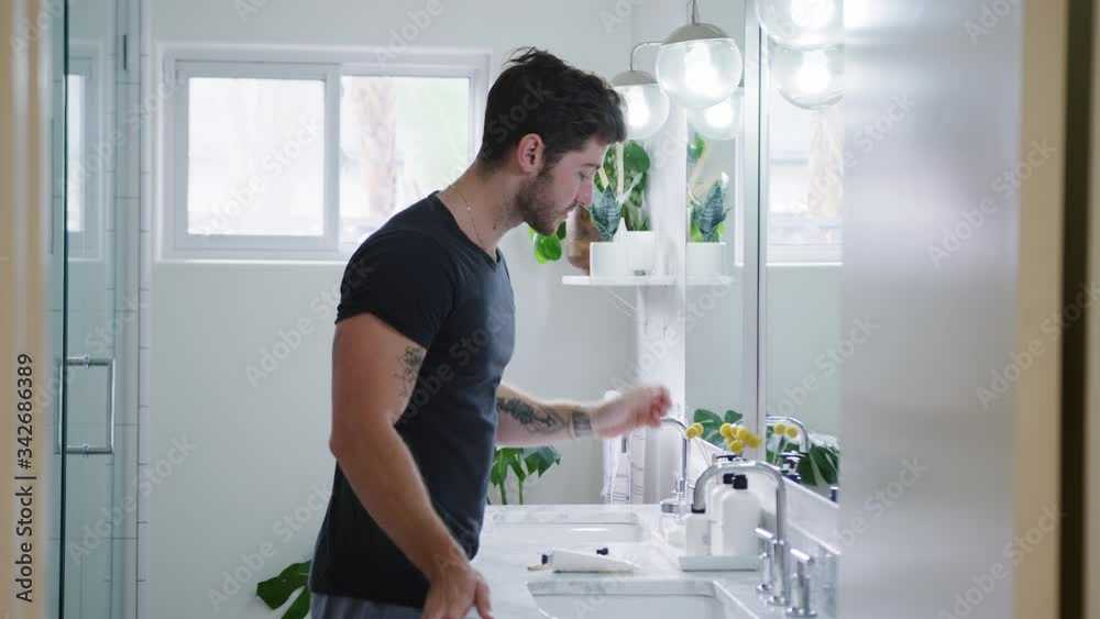 Man Wearing Pyjamas Standing At Sink Putting On Moisturizer In Bathroom