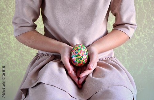 Girl wearing beige dress with colorful , sequin , surprise sparkle egg in hands , easter and spring time , green gold background