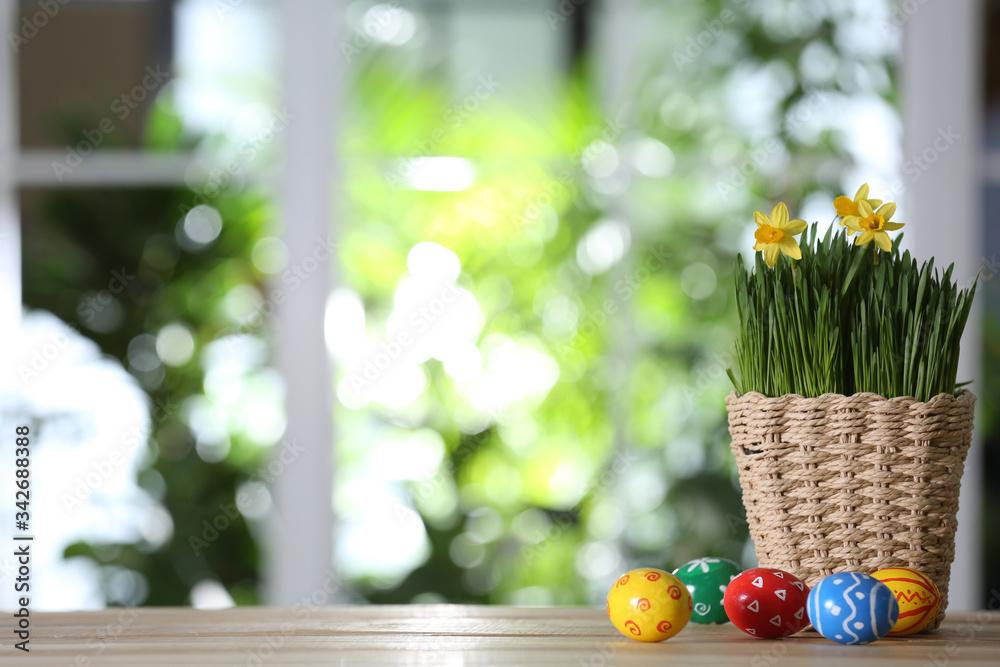 Colorful Easter eggs and flowers on wooden table against blurred green background. Space for text