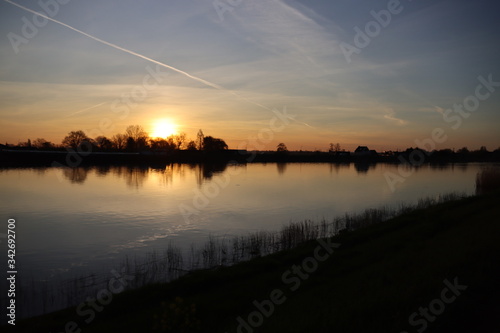 The sun rises over the water of the river Hollandsche IJssel near the dike at Park Hitland