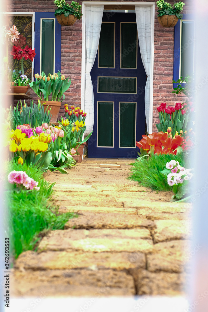 the path from the fence to the house is dotted with flowers tulips on the right and left