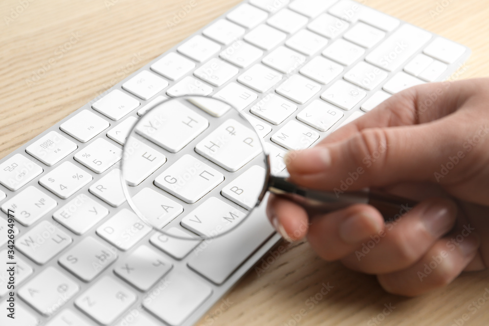 Woman looking through magnifying glass at computer keyboard on table, closeup. Search concept Woman looking through magnifying glass at computer keyboard on table, closeup. Search concept