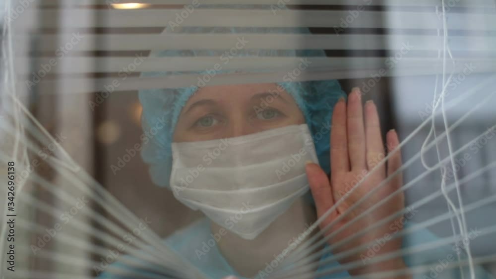 Nurse looking through window of hospital with disturbed look ...