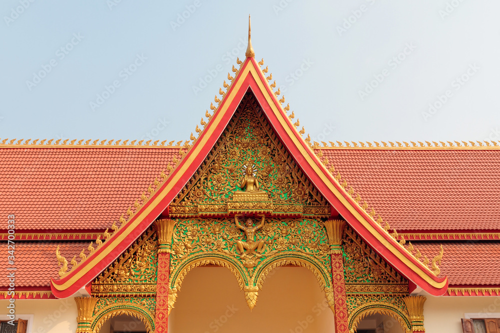 Closeup of the red roof of Buddhist temple with ornate golden decoration in Vientiane in Laos against blue sky Closeup of the red roof of Buddhist temple with ornate golden decoration in Vientiane in Laos against blue sky