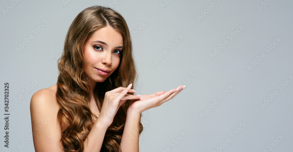 Portrait of young beautiful woman smiles surprise showing product isolated at grey background. Blonde girl with long and shiny wavy hair . Smiling friendly girl with curly hairstyle Portrait of young beautiful woman smiles surprise showing product isolated at grey background. Blonde girl with long and shiny wavy hair . Smiling friendly girl with curly hairstyle