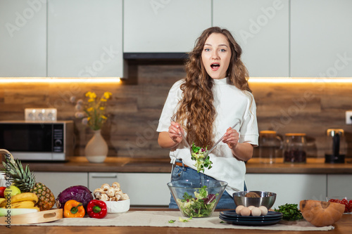 Healthy Food - Vegetable Salad. Diet. Dieting Concept. Young curly woman preparing vegetable salad in her kitchen. Healthy lifestyle concept, beautiful emotional , surprised woman mixed vegetable.