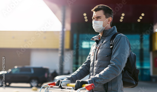 Coronavirus 2020 pandemic. Man in a disposable facial mask and medical gloves with a supermarket cart. Guy goes to the market to buy food during quarantine. Covid 19 epidemic over the World © ANR Production