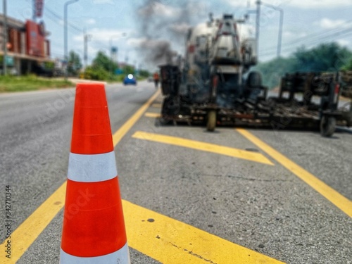 Road maintenance by the ASPHALT HOT MIX IN - PLACE RECYCLING method and with a red cone in the front (blurred image). © suwichan