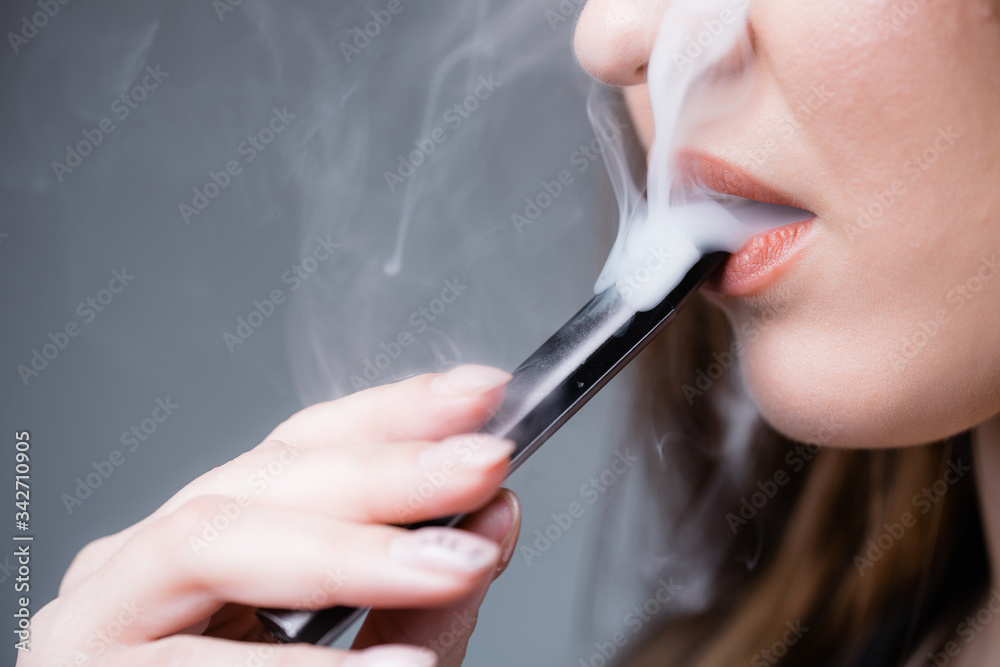 Obraz premium Close-up. The girl smokes an electronic cigarette as a substitute for regular tobacco. Heavy smoke and smoking.