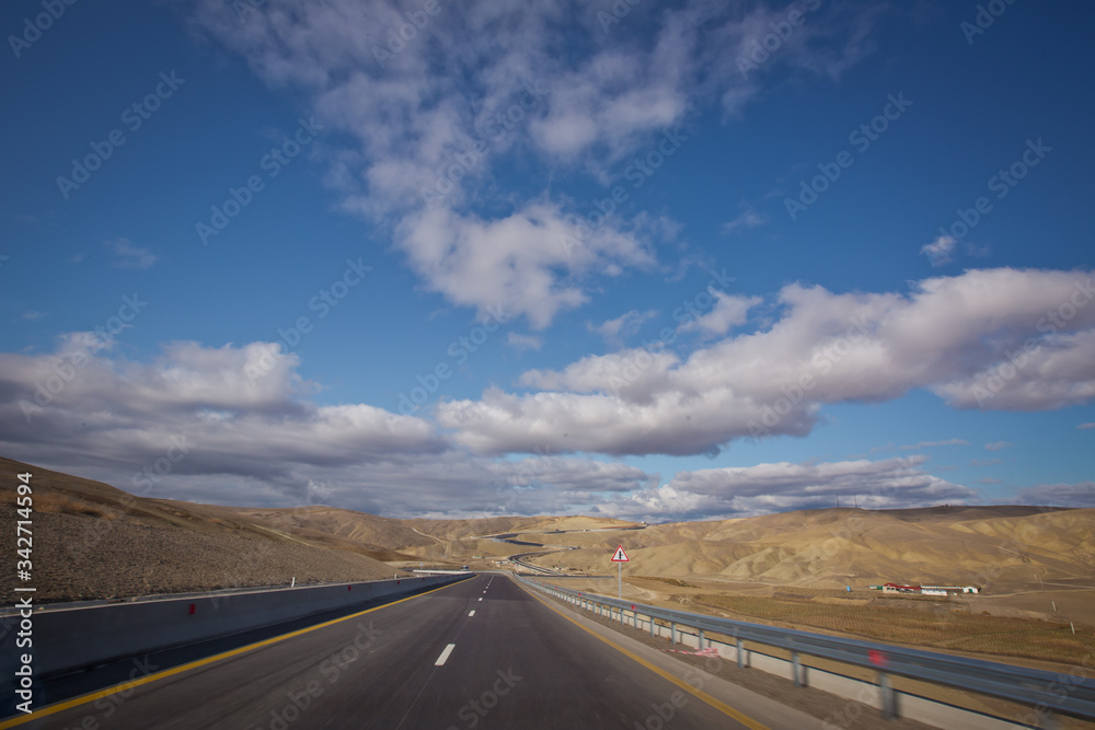 Asphalt road and bright blue sky with fluffy clouds . Empty desert asphalt road from low angle with mountains and clouds on background. road, red desert landscape . Open road with blue clouds . Asphalt road and bright blue sky with fluffy clouds . Empty desert asphalt road from low angle with mountains and clouds on background. road, red desert landscape . Open road with blue clouds .