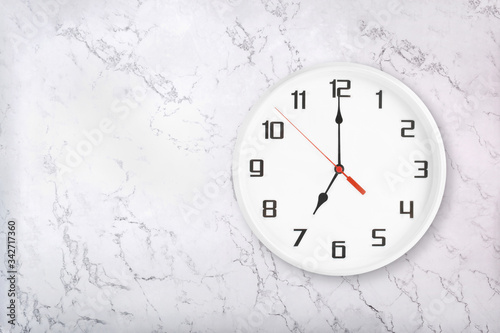 White round wall clock on white natural marble background. Seven o'clock, 7 a.m. or 7 p.m.