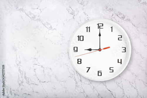 White round wall clock on white natural marble background. Nine o'clock, 9 a.m. or 9 p.m.