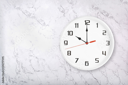 White round wall clock on white natural marble background. Ten o'clock, 10 a.m. or 10 p.m.