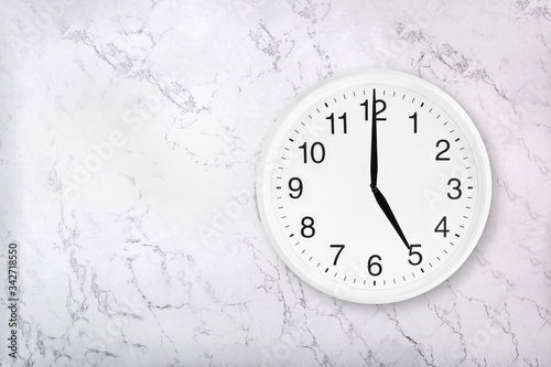 White round wall clock on white natural marble background. Five o'clock. Happy hour. Drinking time. 5 a.m. or 5 p.m