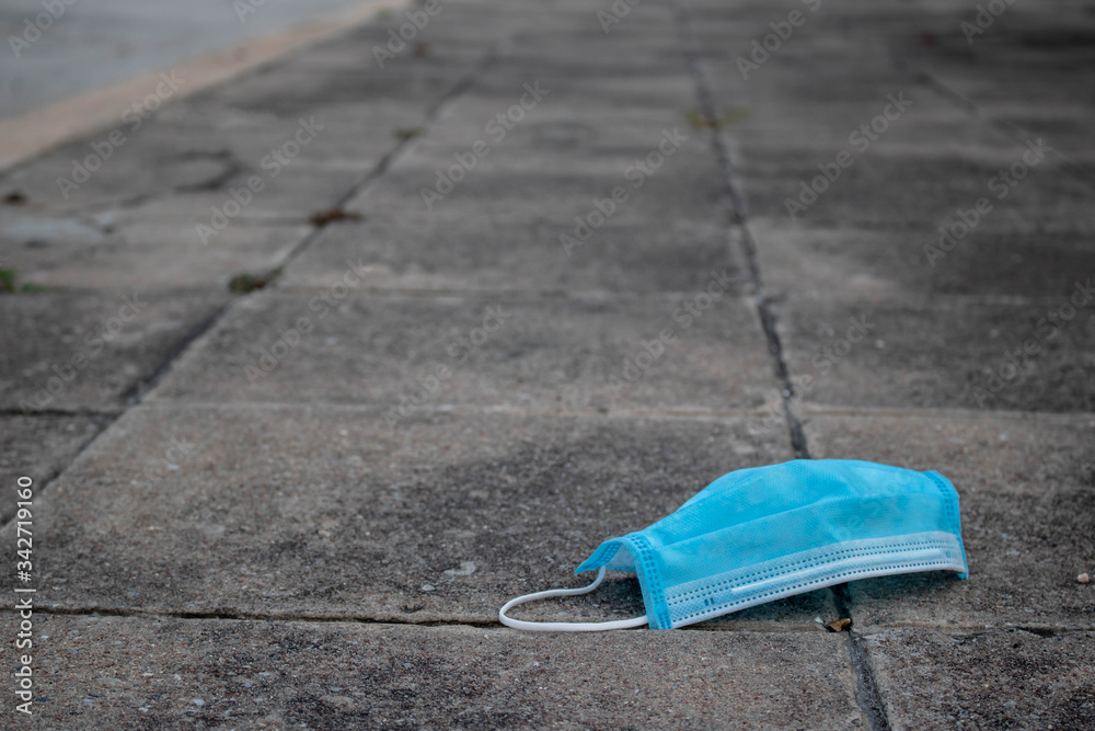 Blue disposable medical mask is on the concrete road surface. to prevent the Virus Covid-19. Concept viruses spread throughout the world. selective fofus. copy space. Blue disposable medical mask is on the concrete road surface. to prevent the Virus Covid-19. Concept viruses spread throughout the world. selective fofus. copy space.