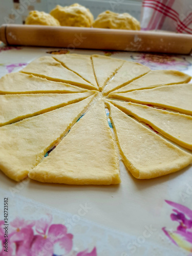 Rolled out dough cut into triangles. Behind it is a rolling pin and three balls of dough. Homemade cooking. Bulgarians put chocolate on the trinagles, roll in and then it is ready for baking. photo
