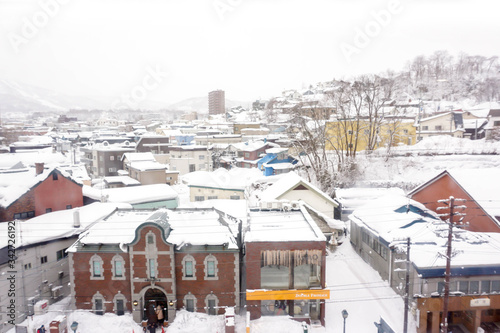 Otaru, Hokkaido prefecture, Japan, February 14 2018 : Closeup and crop high angle view of snow capped Otaru city and Sakaimachi shopping street with tourists on winter foggy sky background.