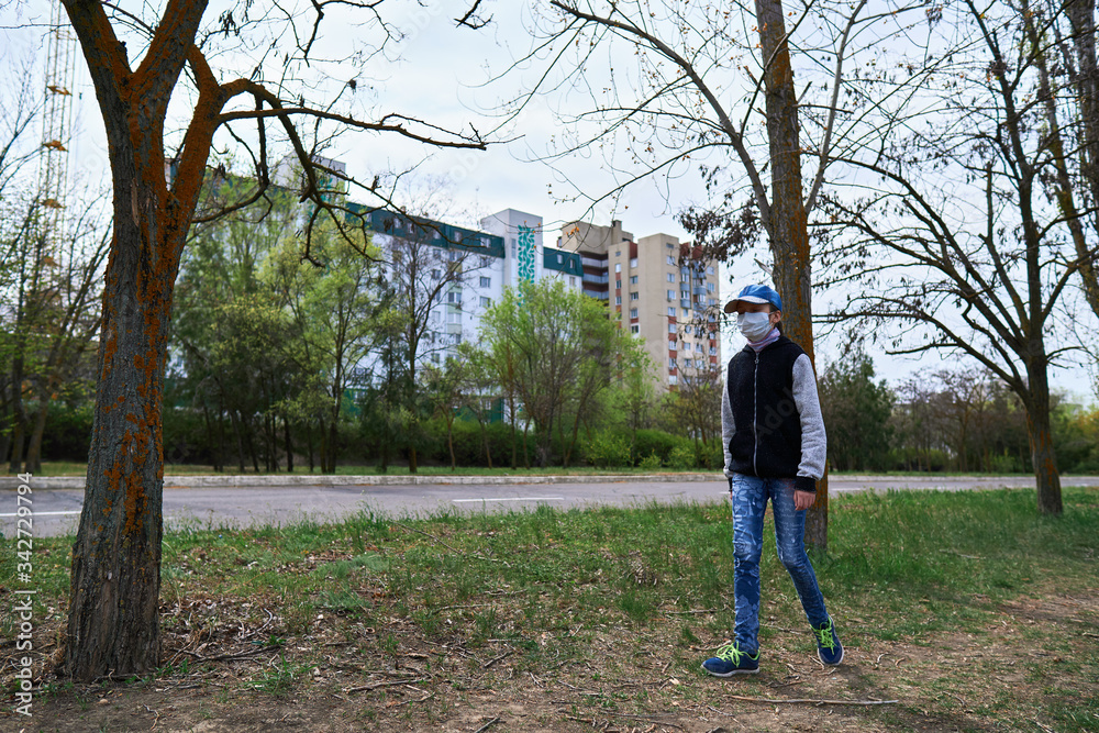 Fototapeta premium child girl walks down the street during the day, a pedestrian walkway and high-rise buildings with apartments, a residential area, a medical mask on her face protects against viruses and dust