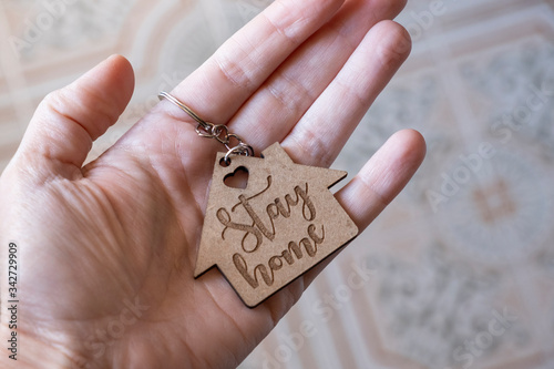 Closeup of a hand holding a wooden keychain with the engraved message stay home