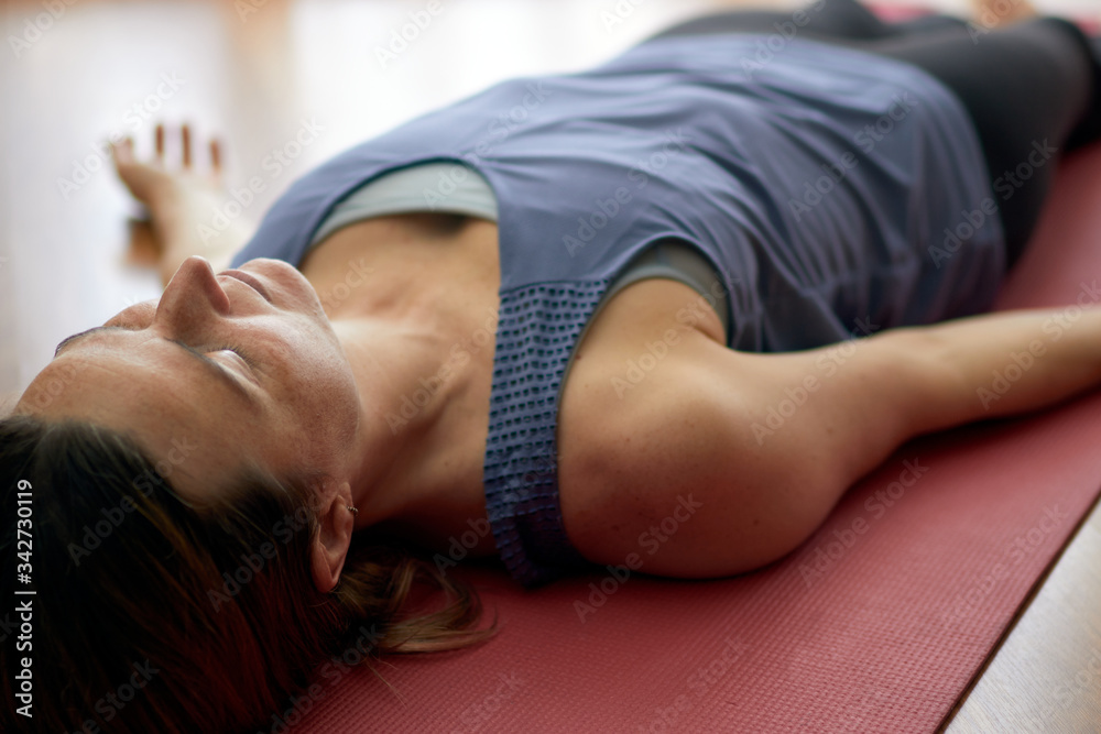 Obraz premium woman practicing yoga, lying in the yoga nidra pose, exercise in Shavasana, exercises, work, rest after practice. Healthy lifestyle concept.