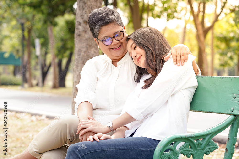 Portrait of elderly mother sitting in the park and her daughter hug her mom with love and care feel happiness, smile, good health and lifestyle. mother day and happy family positive concept