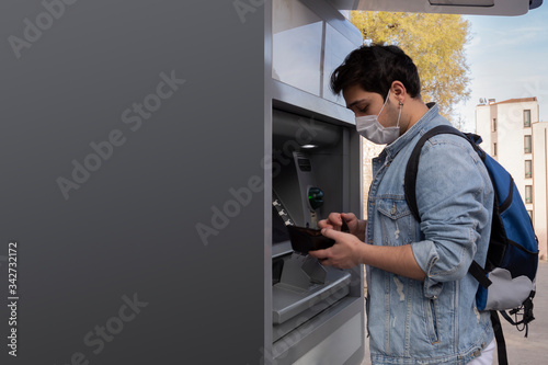 The young man performs his transactions from the bank atm using his protective mask. photo