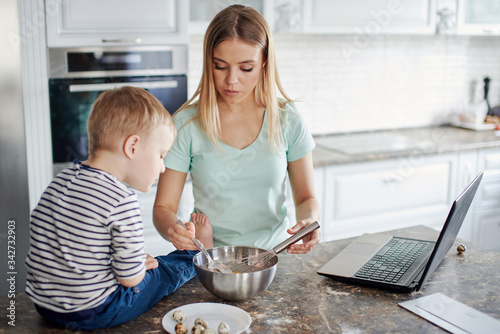 Modern mother cooking with son and using laptop