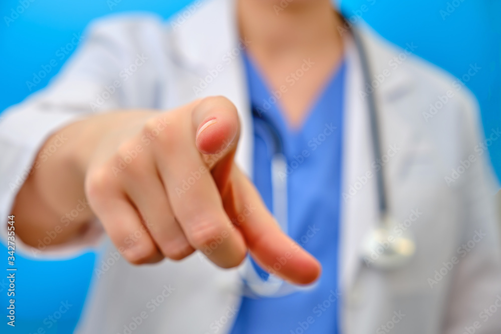 The doctor points his finger forward at you, close-up on a blue background. The nurse gestures with her hand - stay at home. Concept of treatment of the coronavirus epidemic in the world The doctor points his finger forward at you, close-up on a blue background. The nurse gestures with her hand - stay at home. Concept of treatment of the coronavirus epidemic in the world